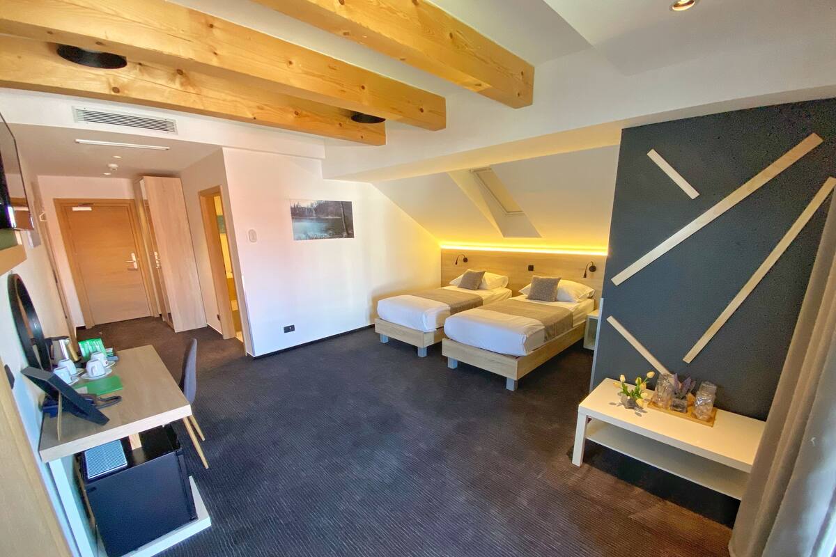 A modern hotel room with two beds, a desk, and a large window.