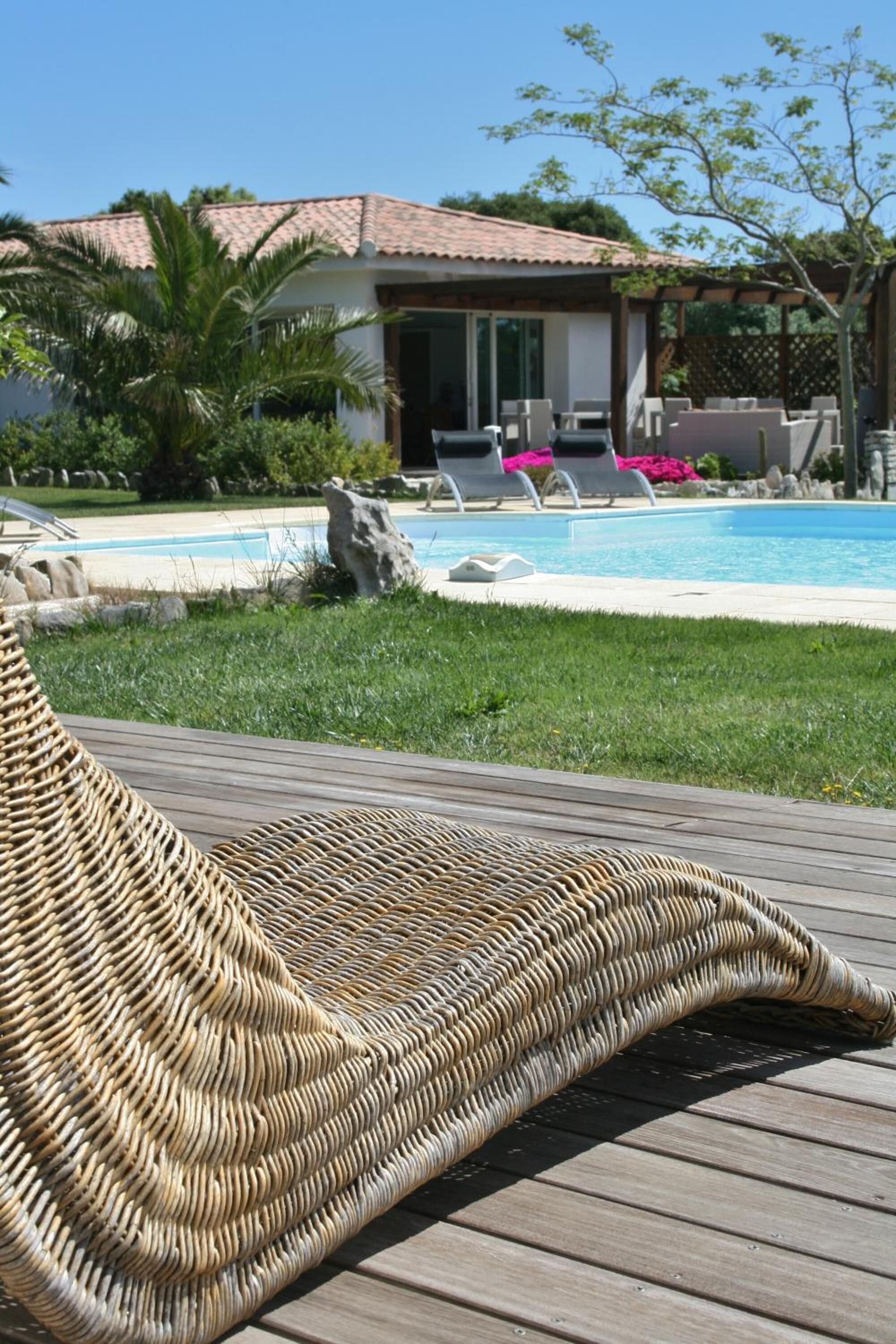 A poolside area with a wicker lounge chair, a pool, and a building with a tiled roof.