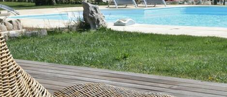 A poolside area with a wicker lounge chair, a pool, and a building with a tiled roof.
