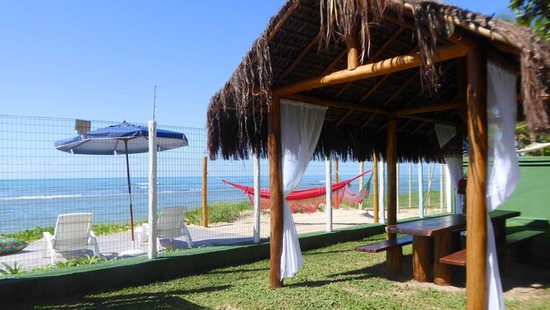 Eine Strandhütte mit einem Reetdach, einer Hängematte und Blick aufs Meer.