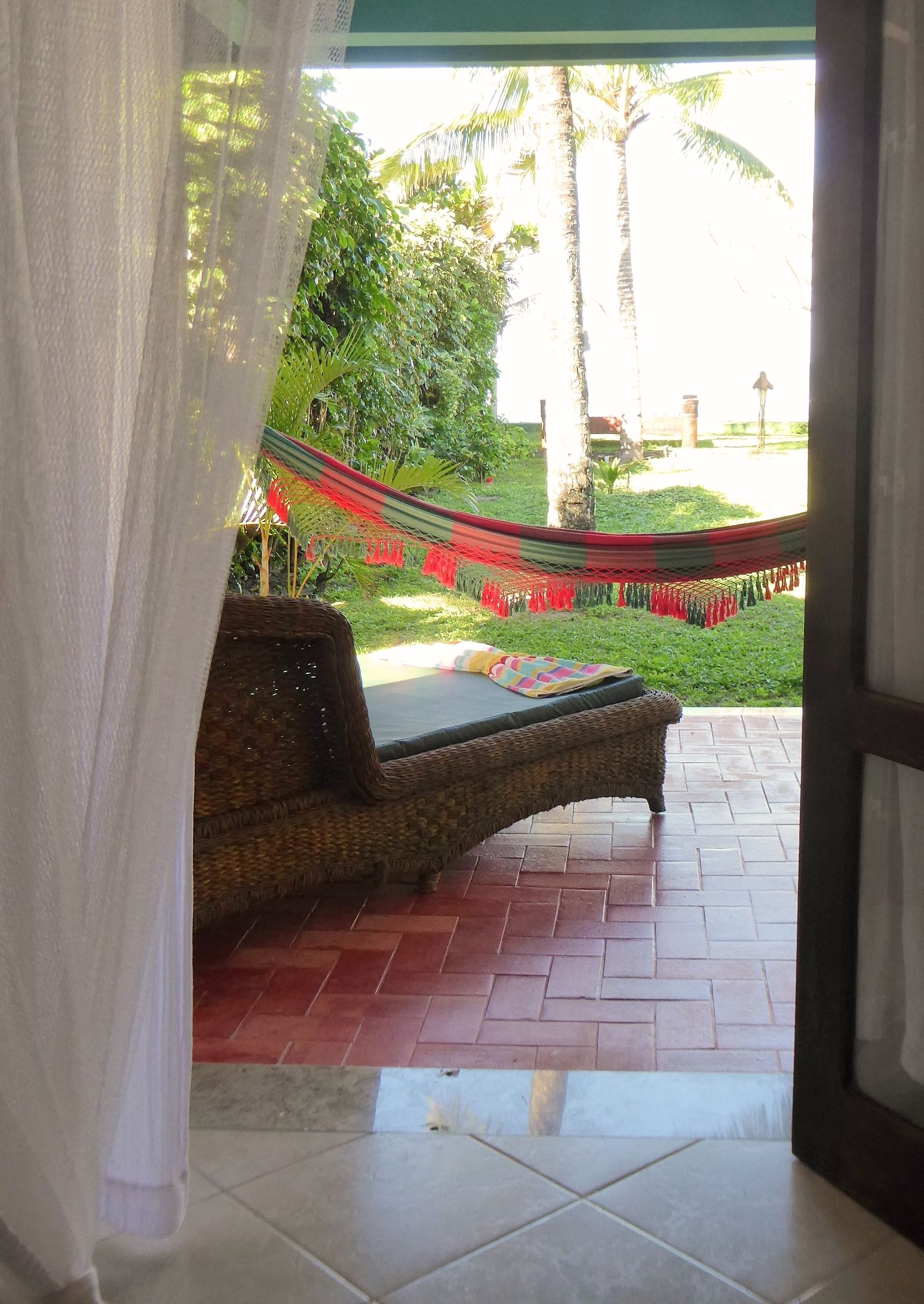 A hammock chair on a tiled patio with a view of a garden and palm trees.