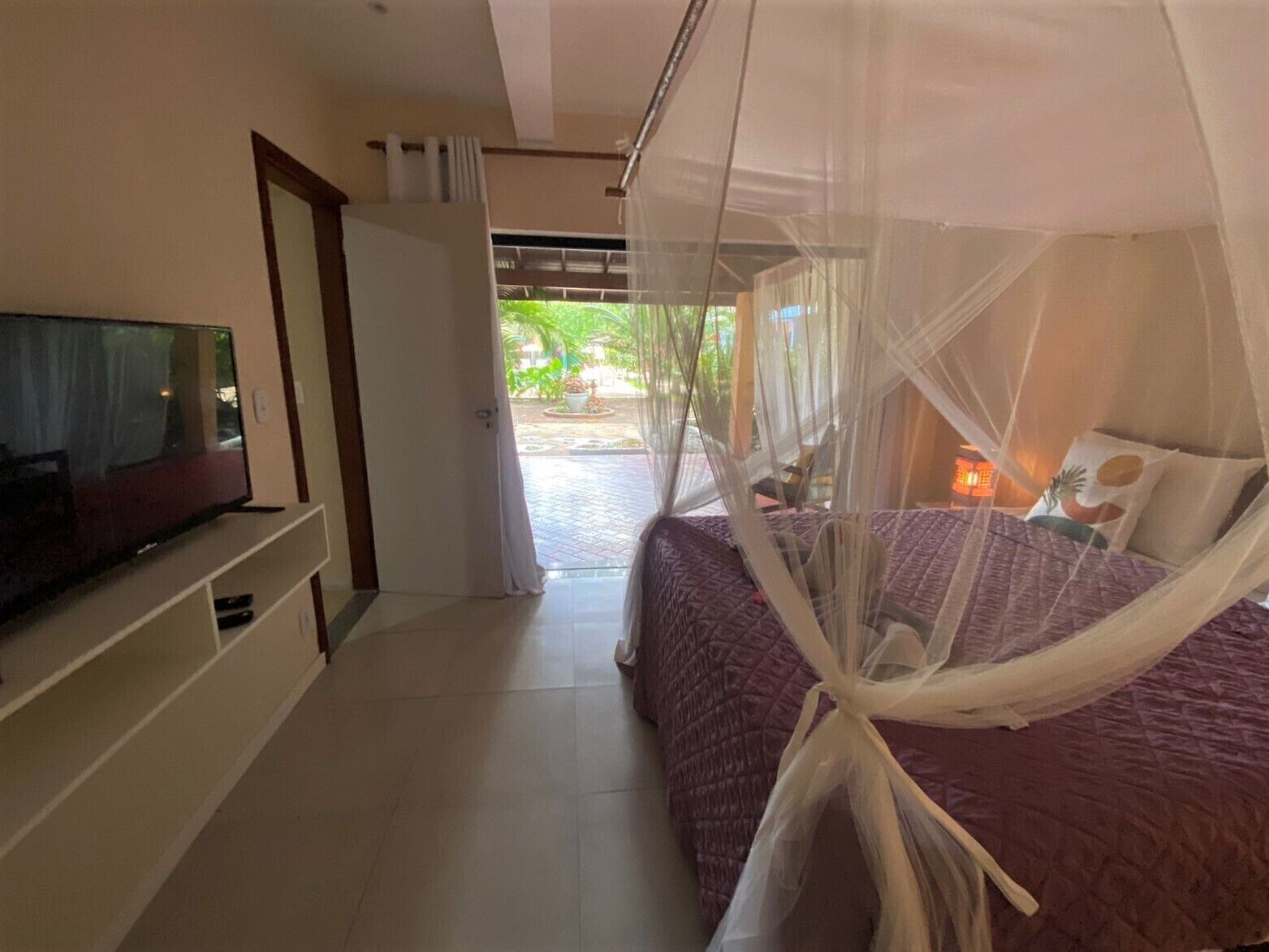 Camera da letto con un letto coperto da una zanzariera, una TV su un mobile e una porta che dà su uno spazio esterno.