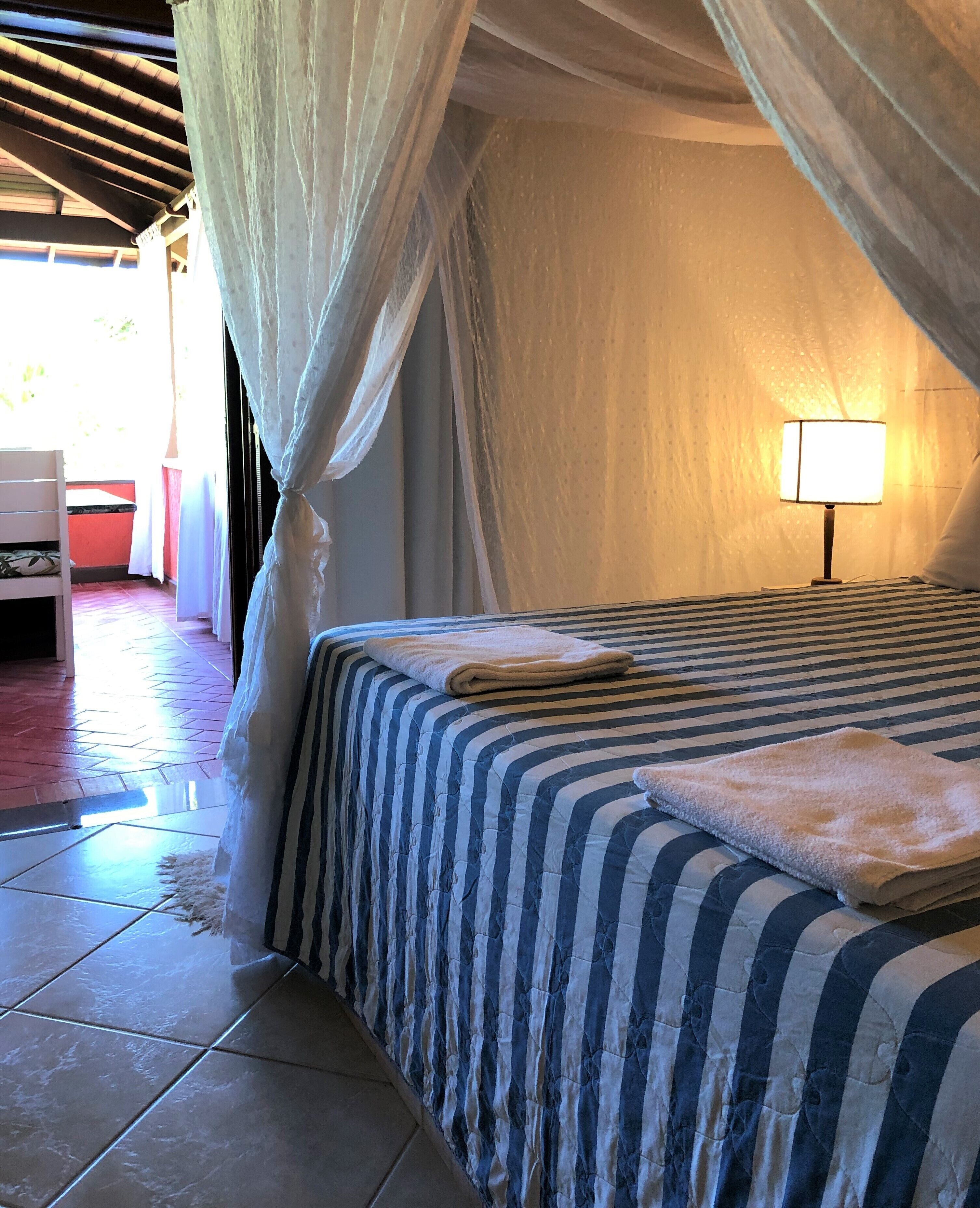 A bedroom with a striped bedspread, a bedside lamp, and a canopy bed.