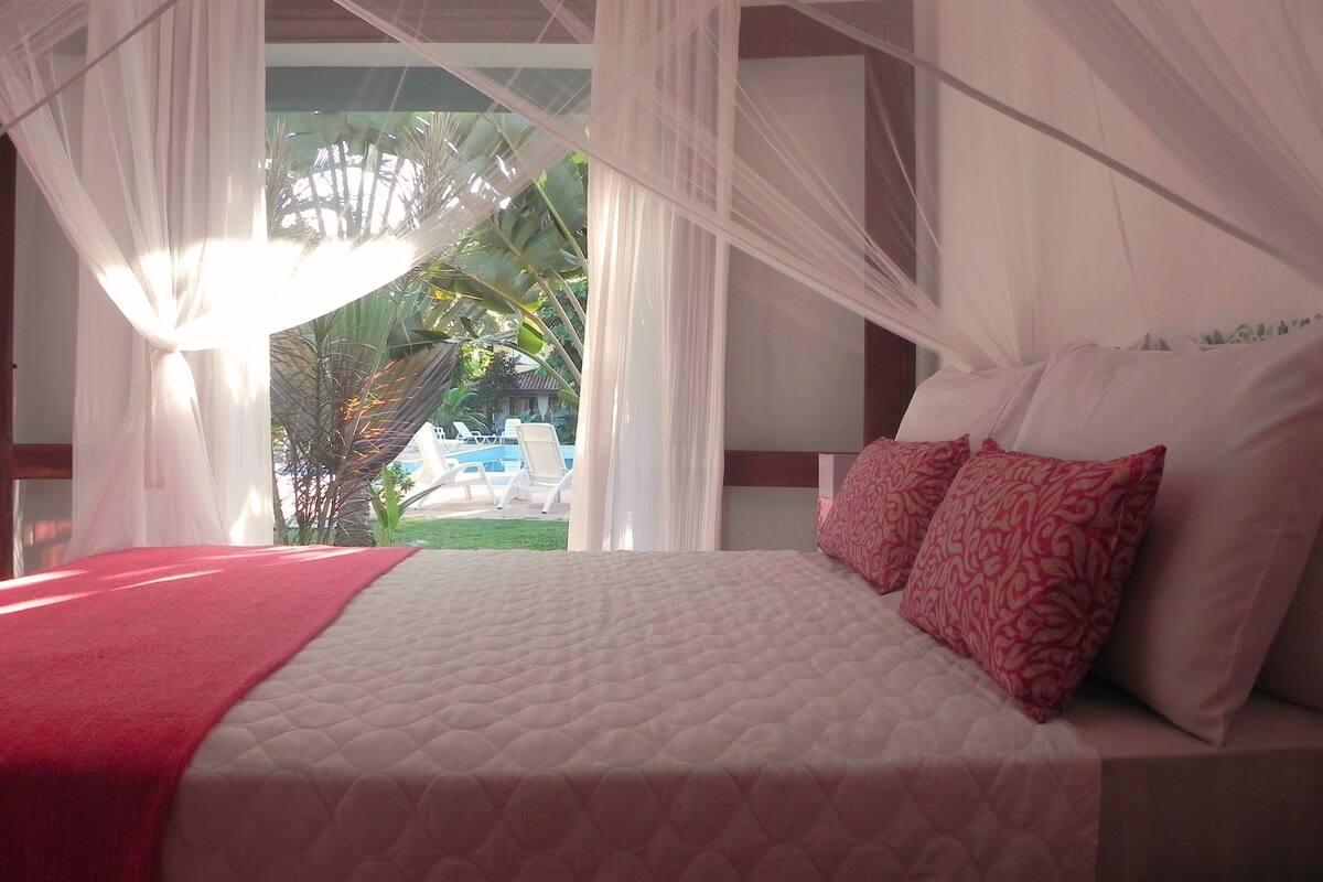 A bed with a red blanket, white pillows, and a canopy.