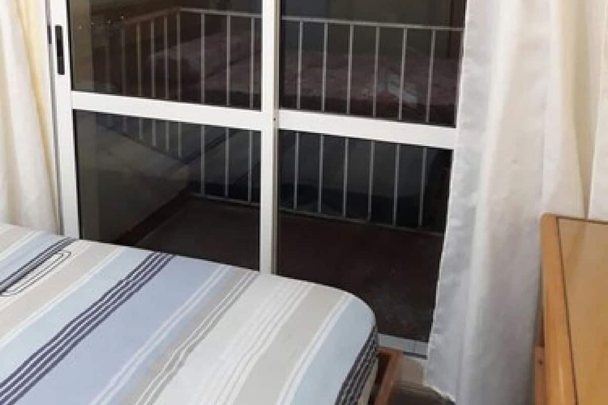 A room with a bed, a sliding glass door to a balcony, and a white curtain.