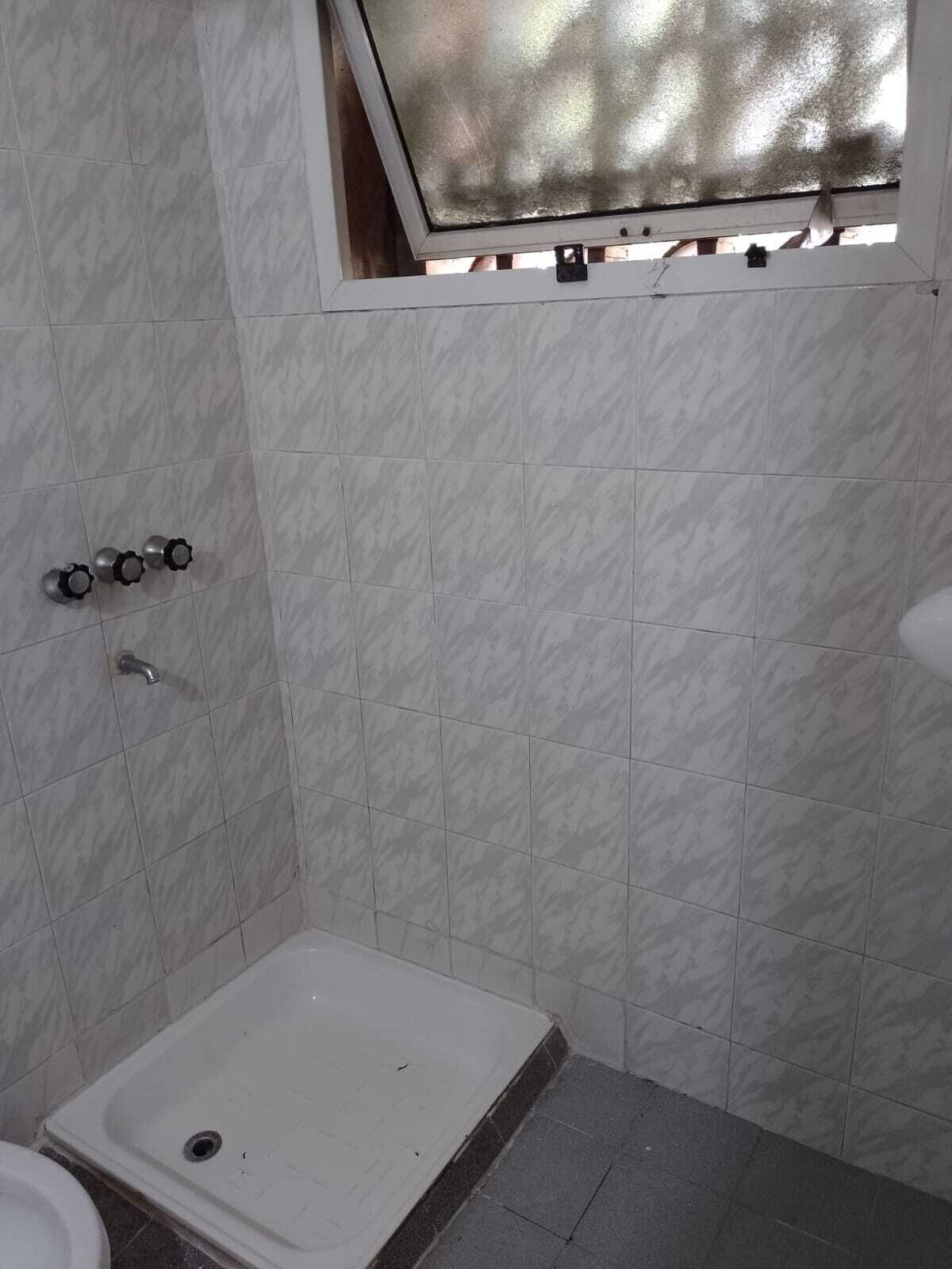 Un baño pequeño con ducha, inodoro y ventana con vidrio esmerilado.