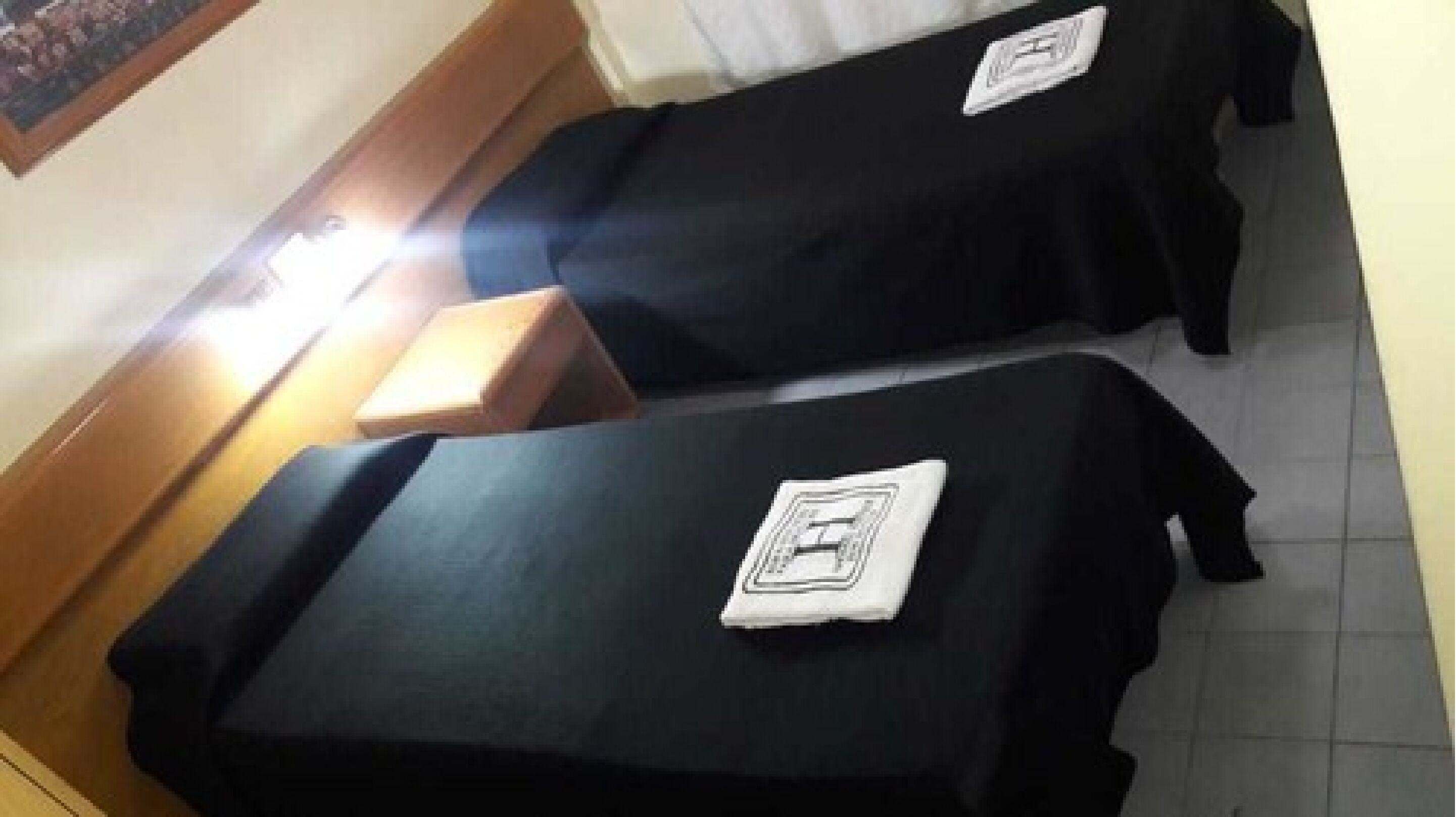Two single beds with black covers and white pillows, a wooden headboard, and a small wooden nightstand.