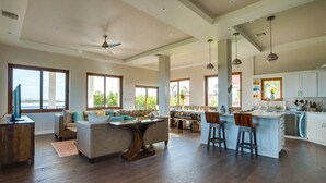 A spacious living area with a large island, a kitchen with white cabinets, and a dining area. - Villa Laguna Gecko (Placencia)