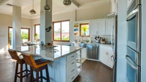 A modern kitchen with white cabinets, a large island with bar stools, stainless steel appliances, and pendant lighting. - Villa Laguna Gecko (Placencia)