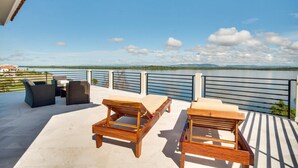 A terrace with wooden lounge chairs and a table, overlooking a body of water and distant mountains. - Villa Laguna Gecko (Placencia)
