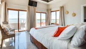 A spacious bedroom with a large bed, a balcony with a view, and a flat-screen TV mounted on the ceiling. - Villa Laguna Gecko (Placencia)