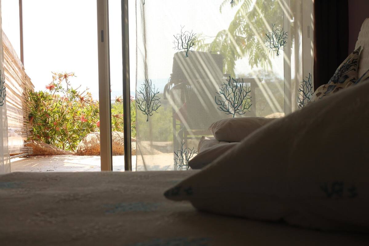 A bedroom with a bed, pillows, and a view of the outdoors through a window.