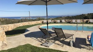 A pool area with a stone wall, two lounge chairs, and an umbrella. - Brise Marine (Bonifacio)