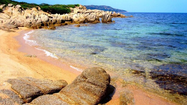 A beach with clear water, rocky formations, and a distant mountain. - Brise Marine (Bonifacio)