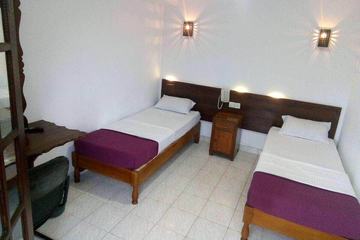 A room with two beds, a desk, and a chair. There are wall-mounted lights and a telephone on the nightstand.