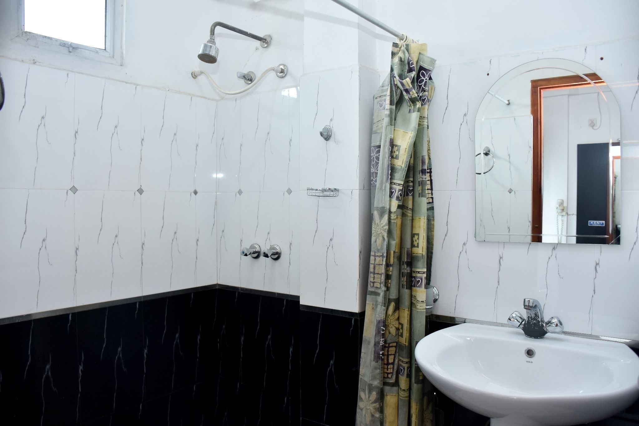 A bathroom with white marble walls, a black marble lower section, a white sink, a shower with a curtain, and a mirror with a wooden frame.