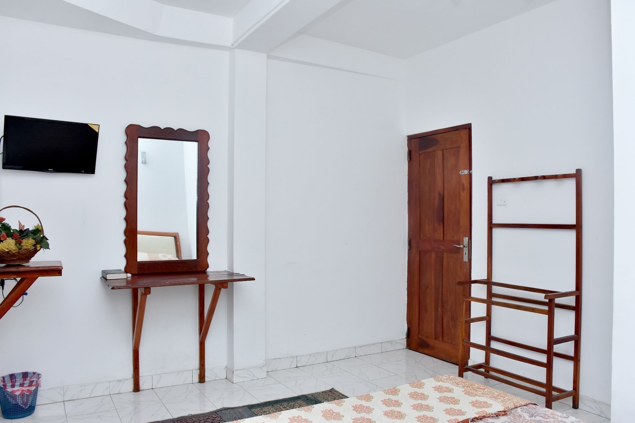 Una habitación con puerta y estante de madera, un espejo y un televisor en la pared.