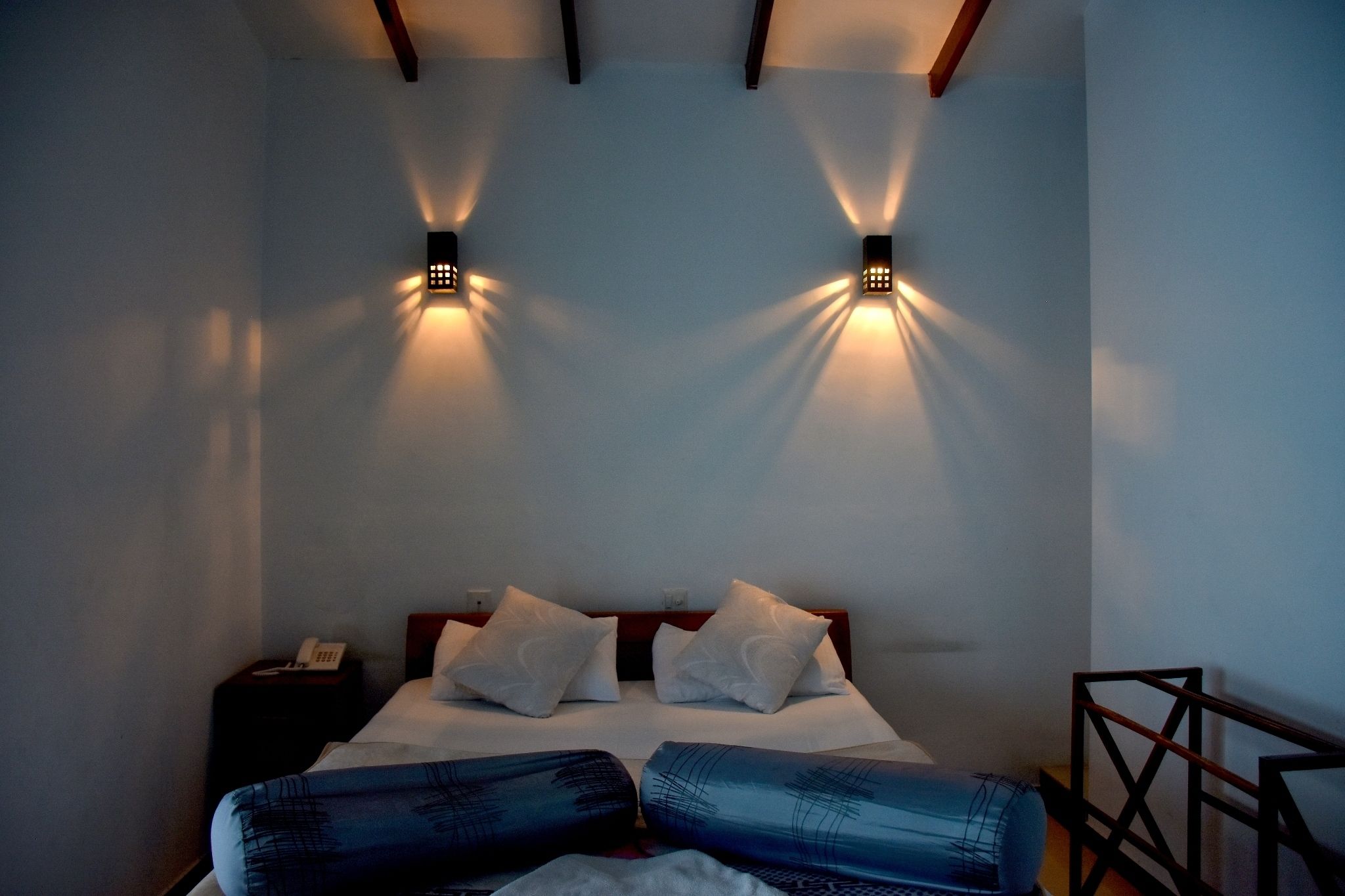 Una habitación de hotel con una cama, dos lámparas de pared, una mesita de noche con un teléfono y un cabecero de madera.