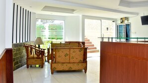 A spacious lobby with a wooden reception desk, a sofa, and a chair. A television is mounted on the wall. - Hotel Hill View (Hatton)