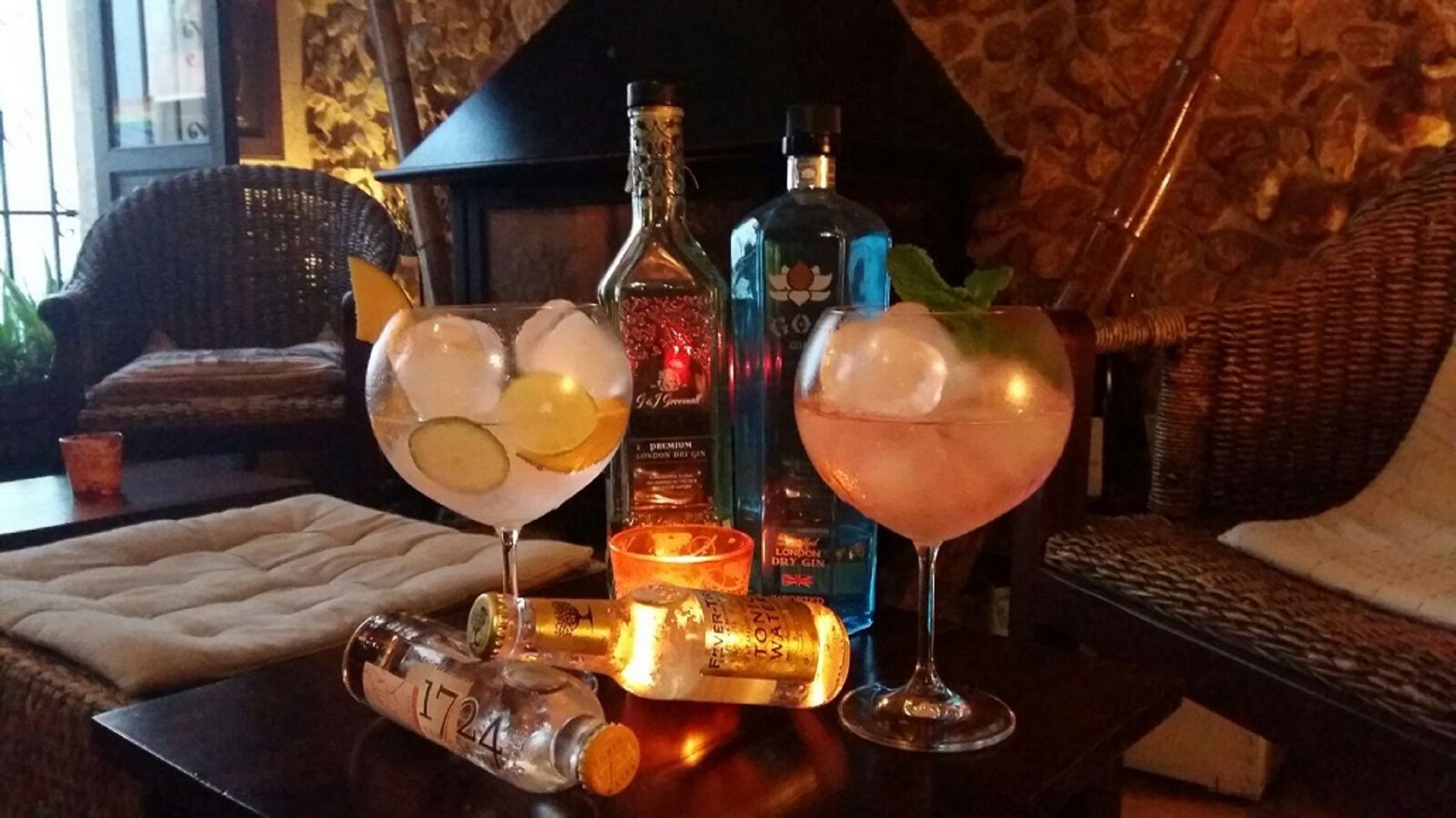 Un’area bar con due cocktail, una bottiglia di gin e una bottiglia di acqua tonica su un tavolo.
