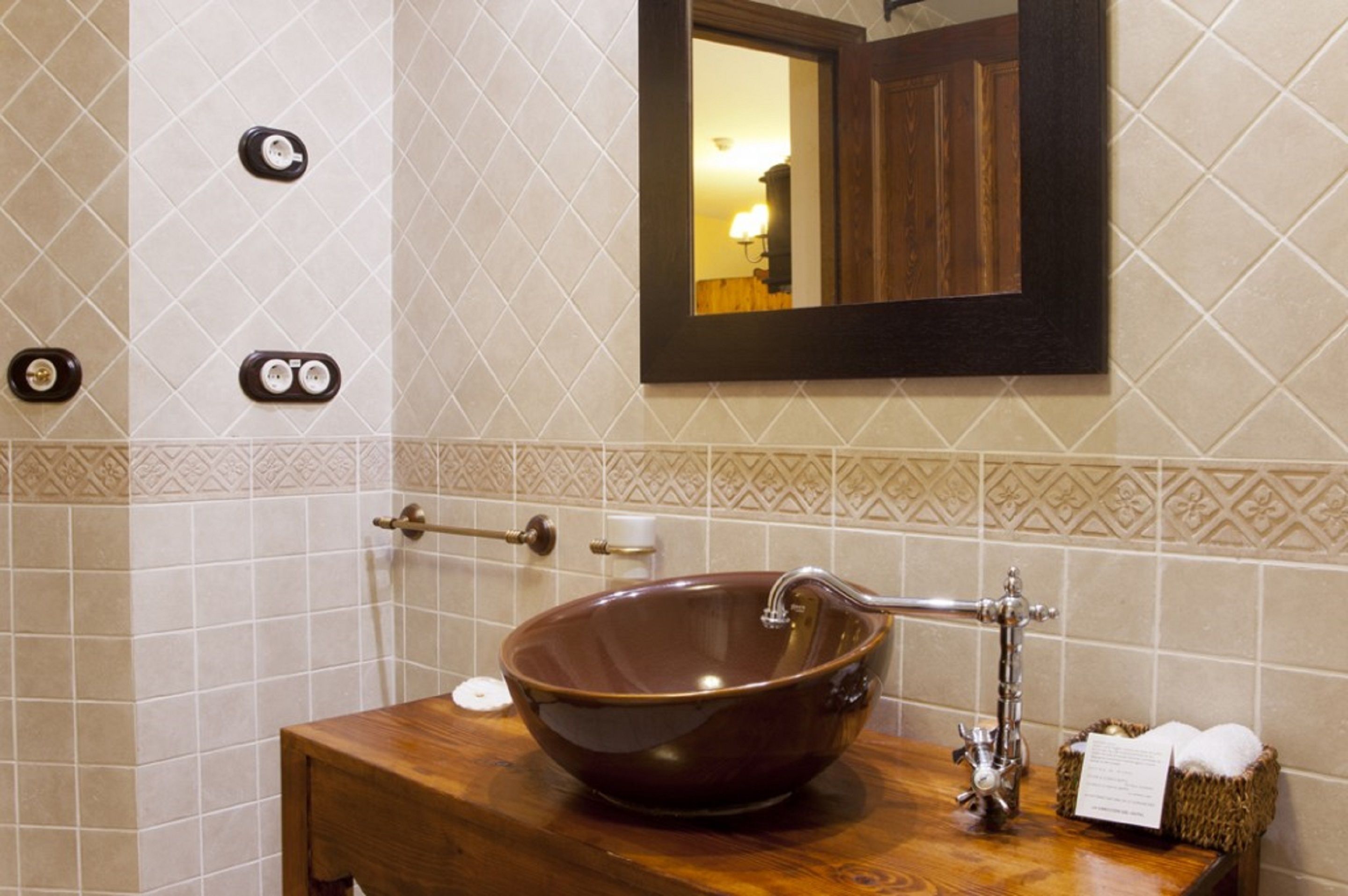 A bathroom with a wooden vanity, a large vessel sink, a towel rack, and a mirror.