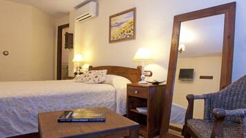 A hotel room with two beds, a wooden table, a chair, a nightstand with a lamp, and a painting on the wall.