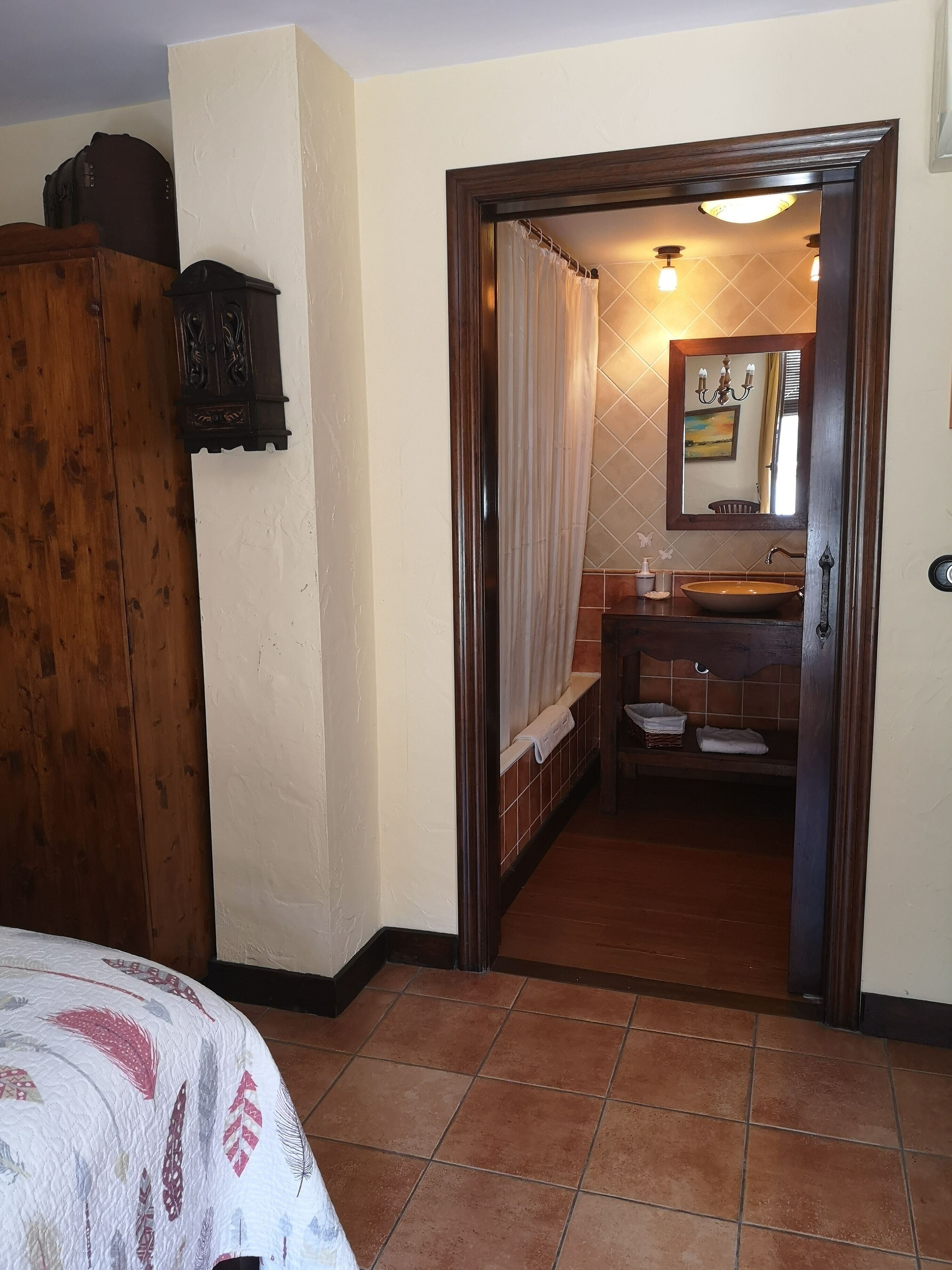 A room with a bed, a wooden wardrobe, a bathroom with a sink, and a mirror.