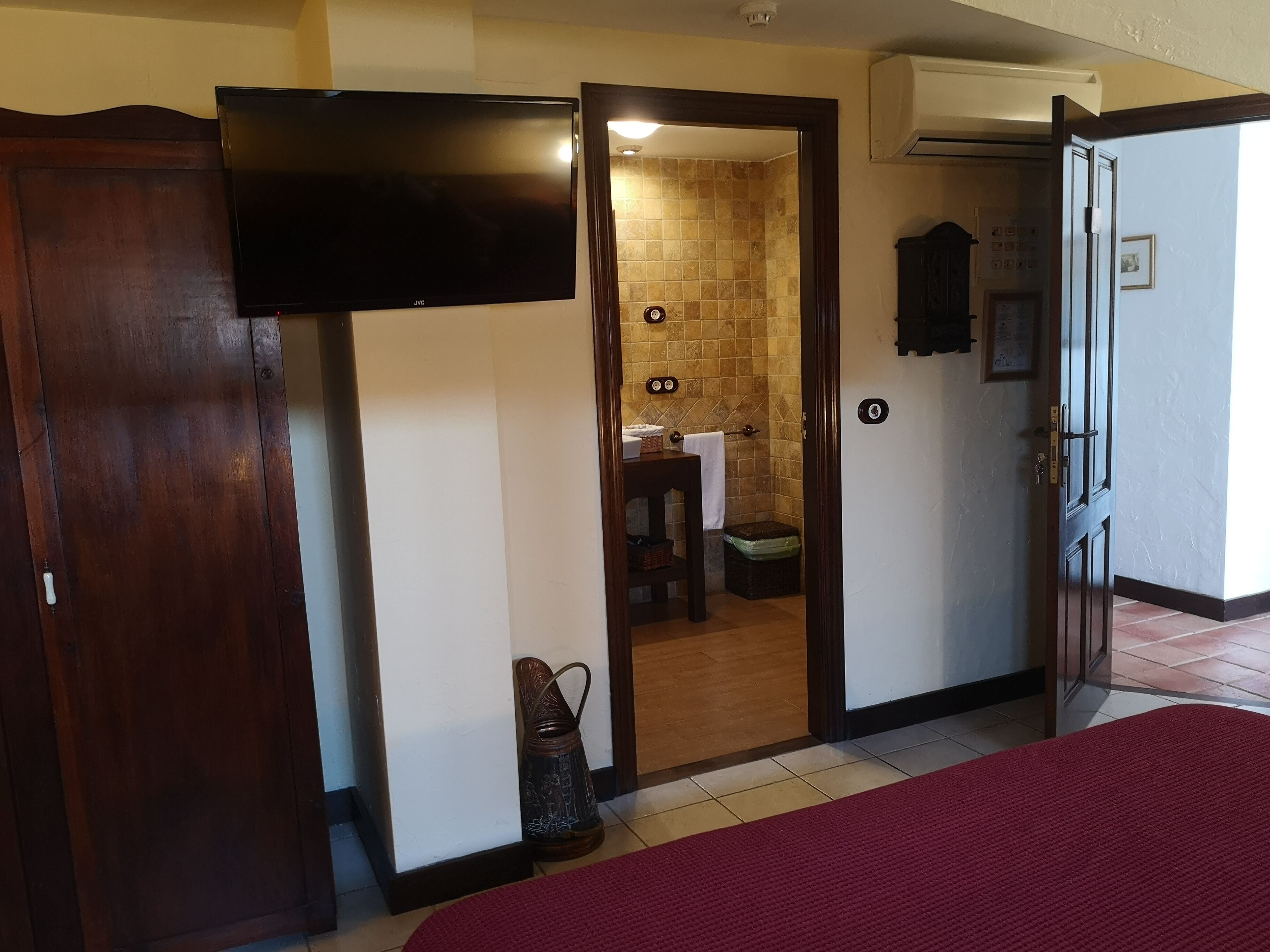 A hotel room with a wooden door, a TV, a red carpet, and a bathroom visible through an open door.