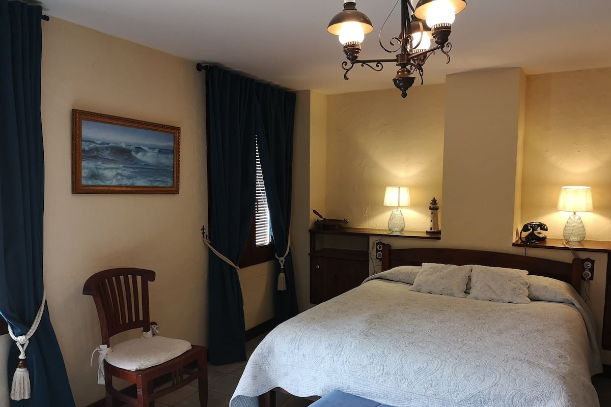 Quarto de hotel com cama, poltrona, escrivaninha com luminária, quadro e lustre.