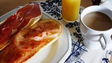 Un plato con jamón serrano, rodajas de tomate y un vaso de zumo de naranja sobre una mesa con una taza blanca.