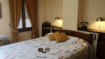 A hotel room with a bed, two bedside lamps, a wooden nightstand, a mirror, and a window with curtains.