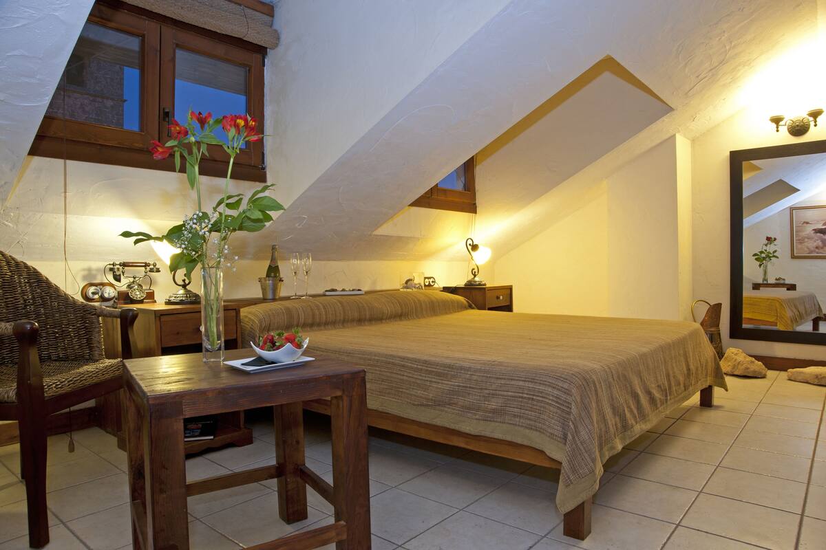 Quarto com uma cama grande, uma mesa de madeira, um vaso com flores e uma janela com cortinas.