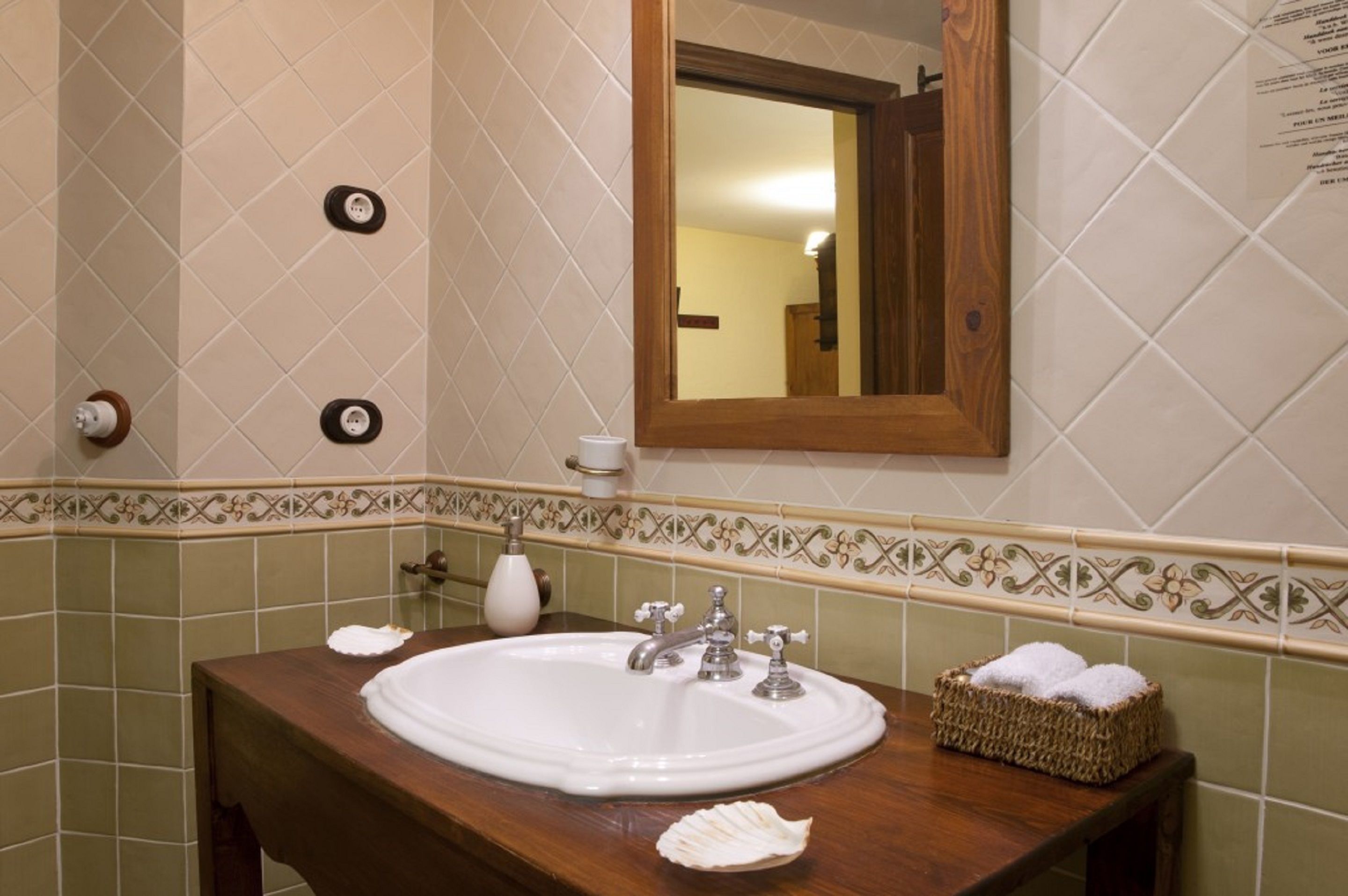 A bathroom with a wooden vanity, a white sink, a mirror, and a decorative tile border.