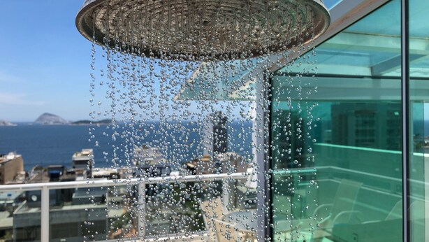 A modern showerhead with water droplets on a glass window overlooking a cityscape and sea. - My Rio Penthouse Ipanema Beach (Rio de Janeiro)