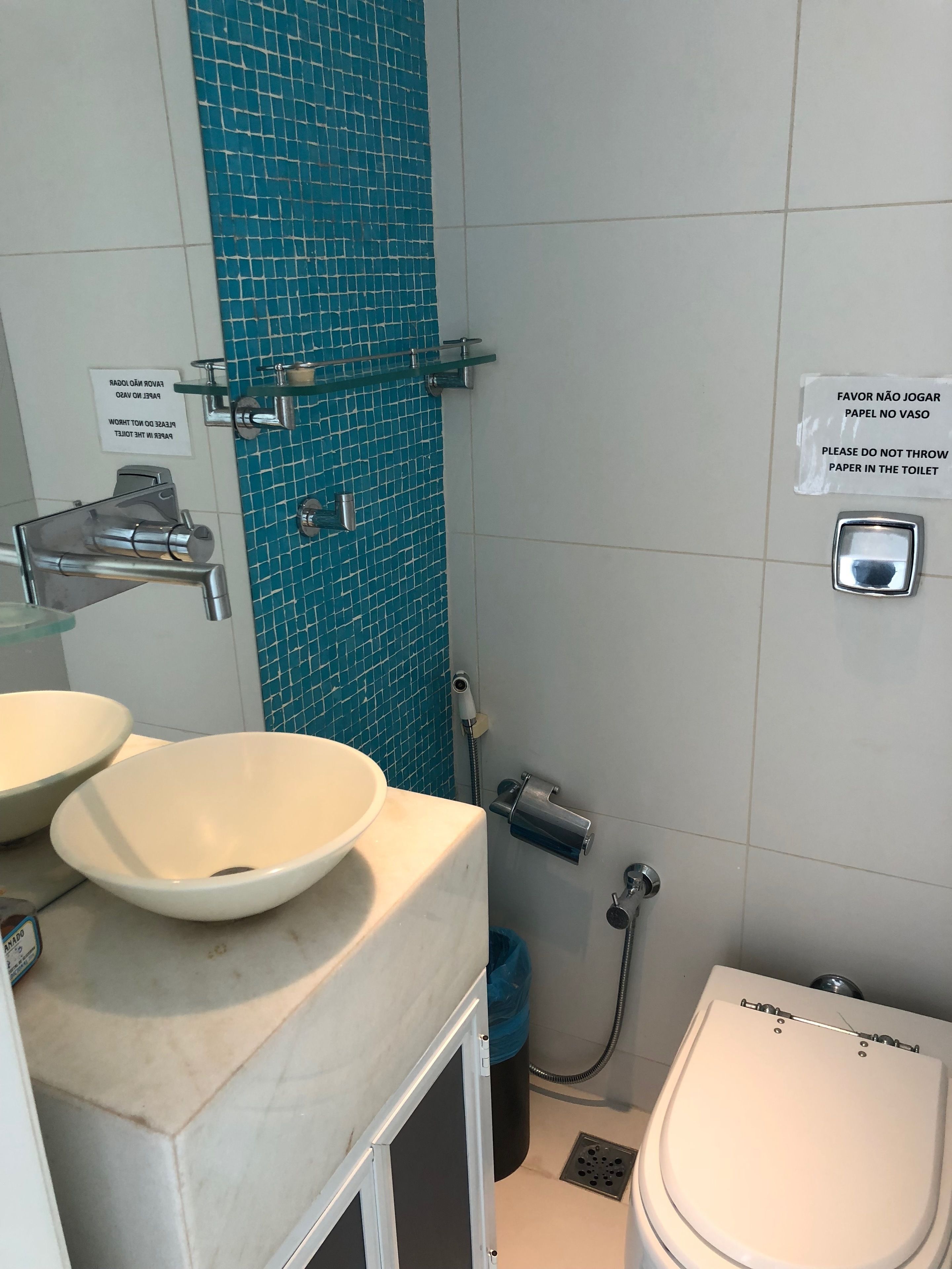 Baño con lavamanos, espejo e inodoro. Se observan letreros en un idioma extranjero y una zona de ducha.
