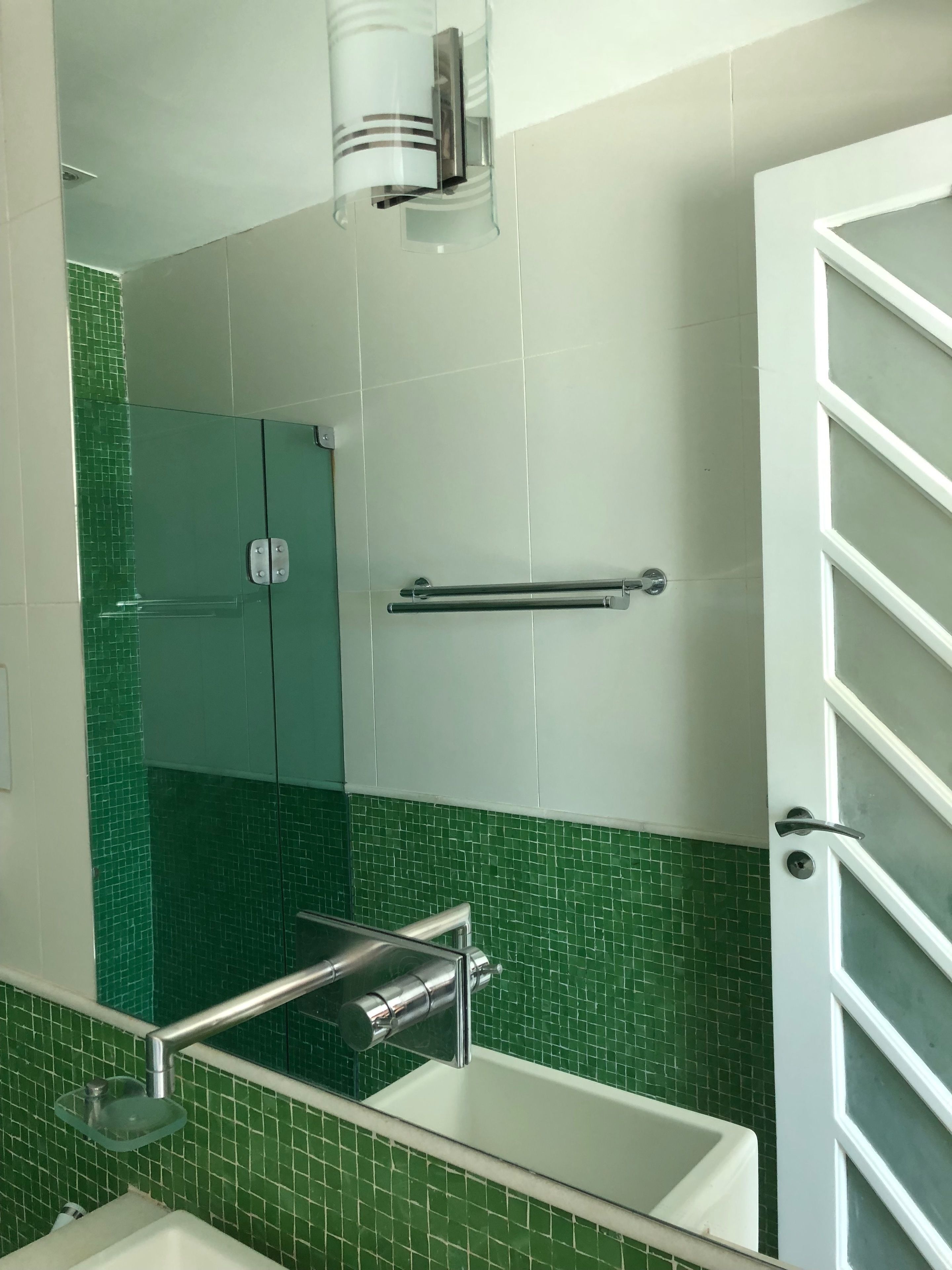 Un baño con cabina de ducha de vidrio, un lavamanos blanco y una pared con azulejos verdes.