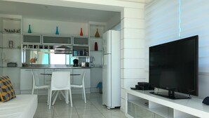 A modern kitchen with white cabinetry, a dining area with white chairs, and a large flat-screen TV on a white stand. - My Rio Penthouse Ipanema Beach (Rio de Janeiro)