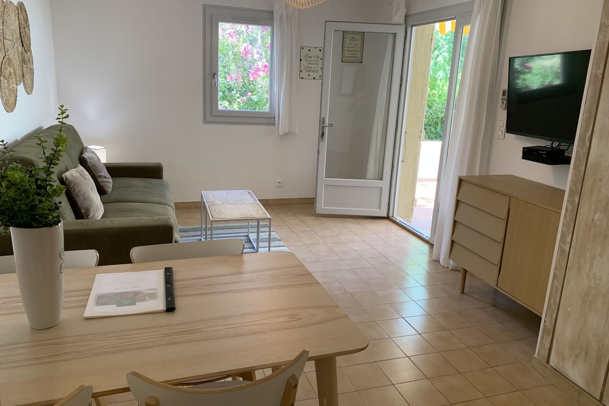 Sala de estar com sofá, mesa de centro, televisão e porta de vidro deslizante para área externa.
