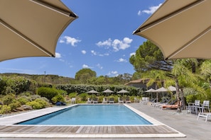 Una piscina con sillones de descanso y sombrillas, rodeada de follaje y árboles.
