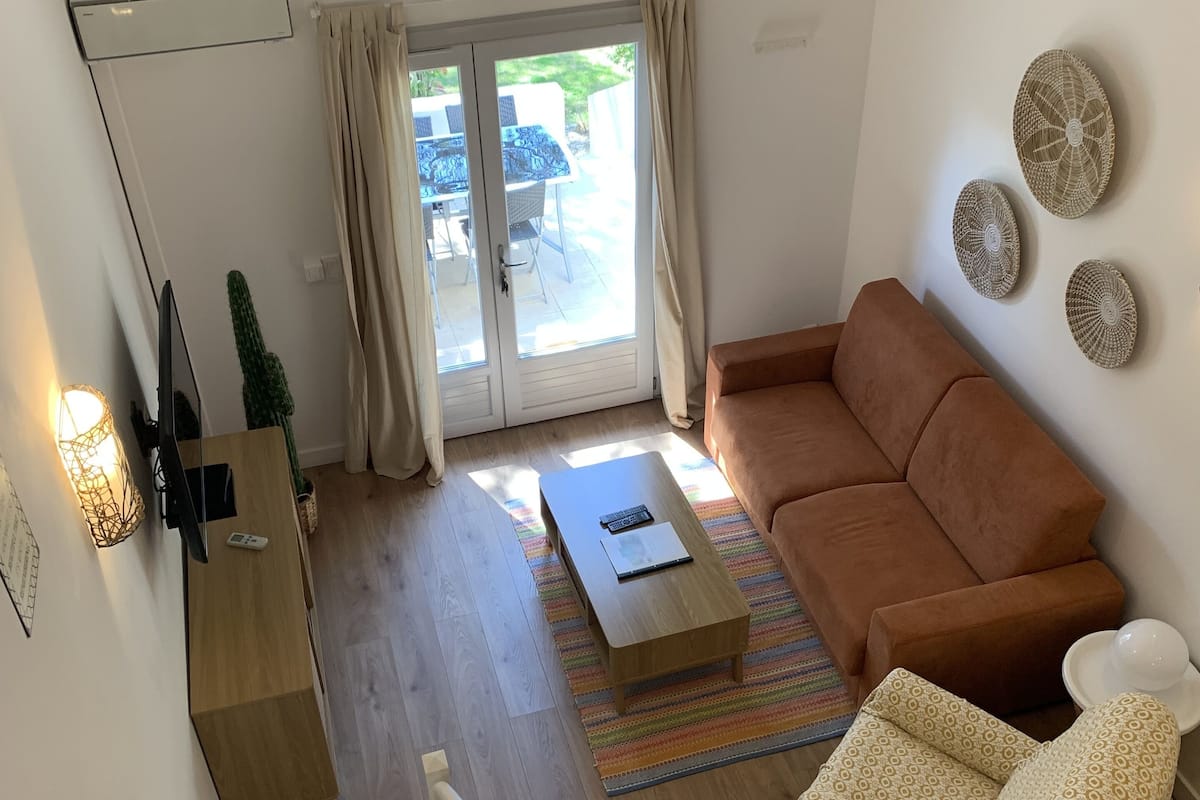 Uma sala de estar com um sofá marrom, uma mesa de centro de madeira e uma escada que leva a um andar superior.