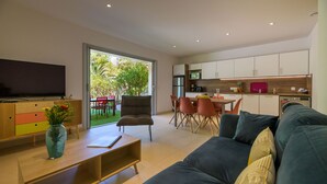 A modern living room with a sofa, a coffee table, and a TV. There is a dining area with chairs and a table, and a kitchen with cabinets and appliances. - Les Pins de Santa Giulia (Porto-Vecchio)