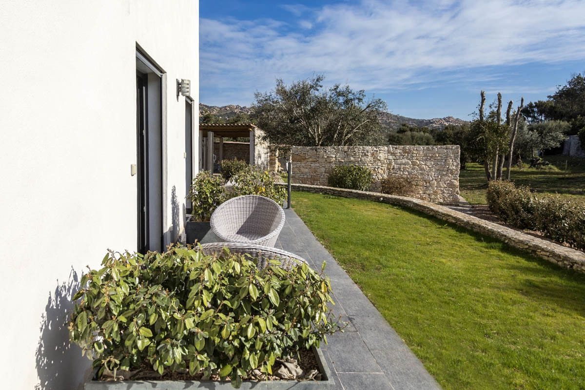 A modern outdoor area with a stone wall, a grassy lawn, and a wicker chair.