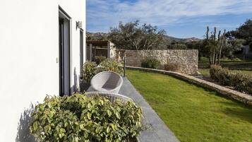 A modern outdoor area with a stone wall, a grassy lawn, and a wicker chair.