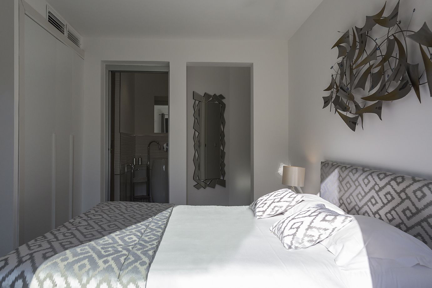 Een slaapkamer met een bed, een spiegel en een decoratief object aan de muur.