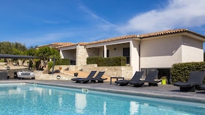A poolside area with lounge chairs and a stone building with a tiled roof. - L'Albitru (Bonifacio)