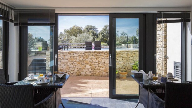 A modern outdoor dining area with a stone wall and glass doors leading to a patio. - L'Albitru (Bonifacio)