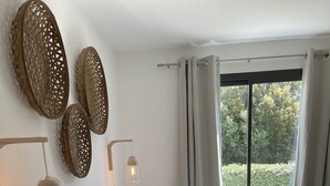 A bedroom with a large bed, patterned pillows, a hanging light fixture, and a view of greenery outside. - L'Albitru (Bonifacio)