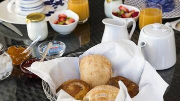 Desayuno con pastelería, una cafetera y cuencos de fruta sobre una mesa.