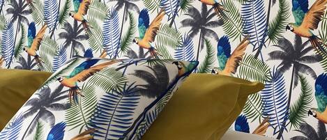 A bed with white bedding and green pillows, set against a wall with a tropical leaf and bird pattern.
