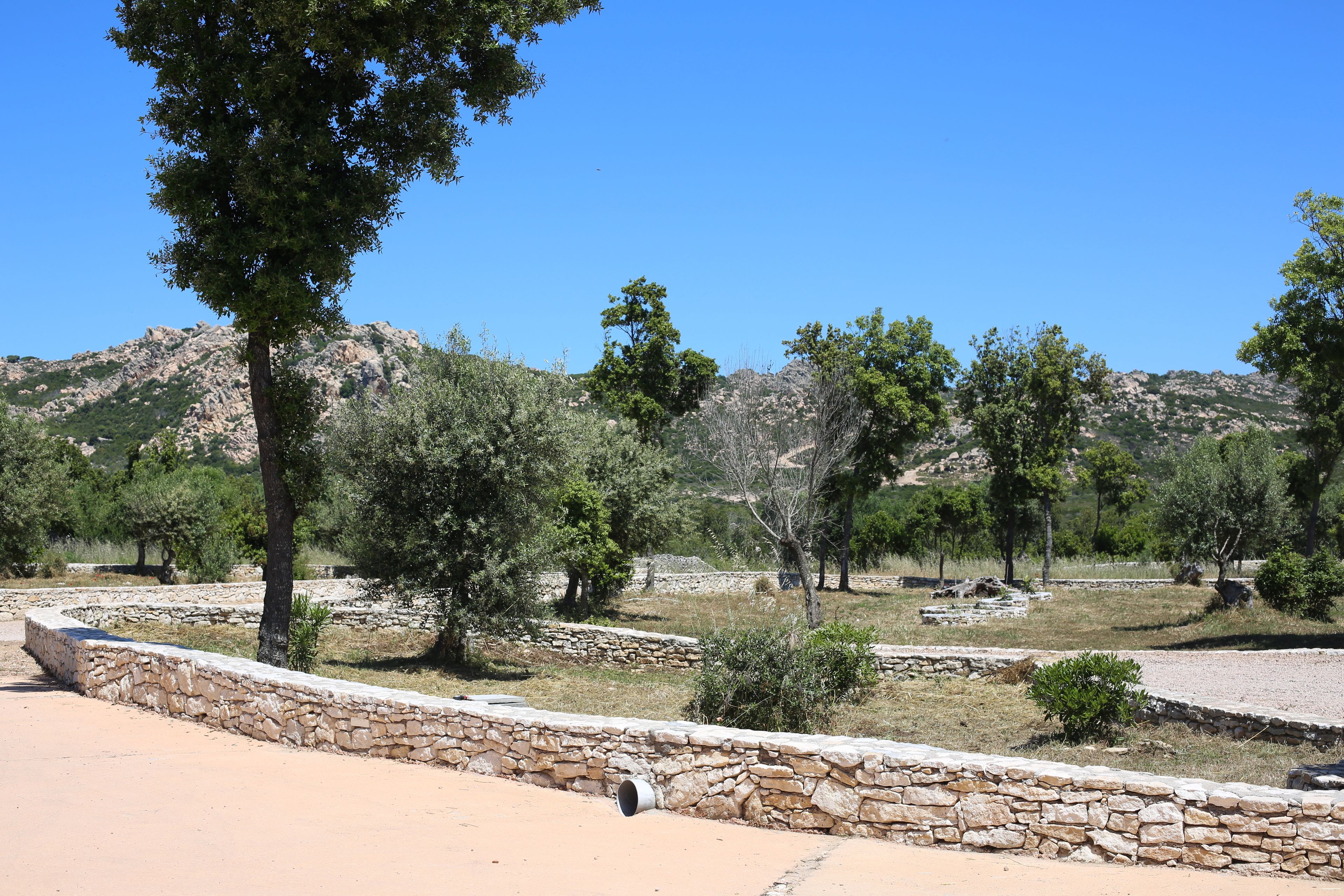A stone wall with a circular opening, surrounded by trees and a mountainous backdrop.